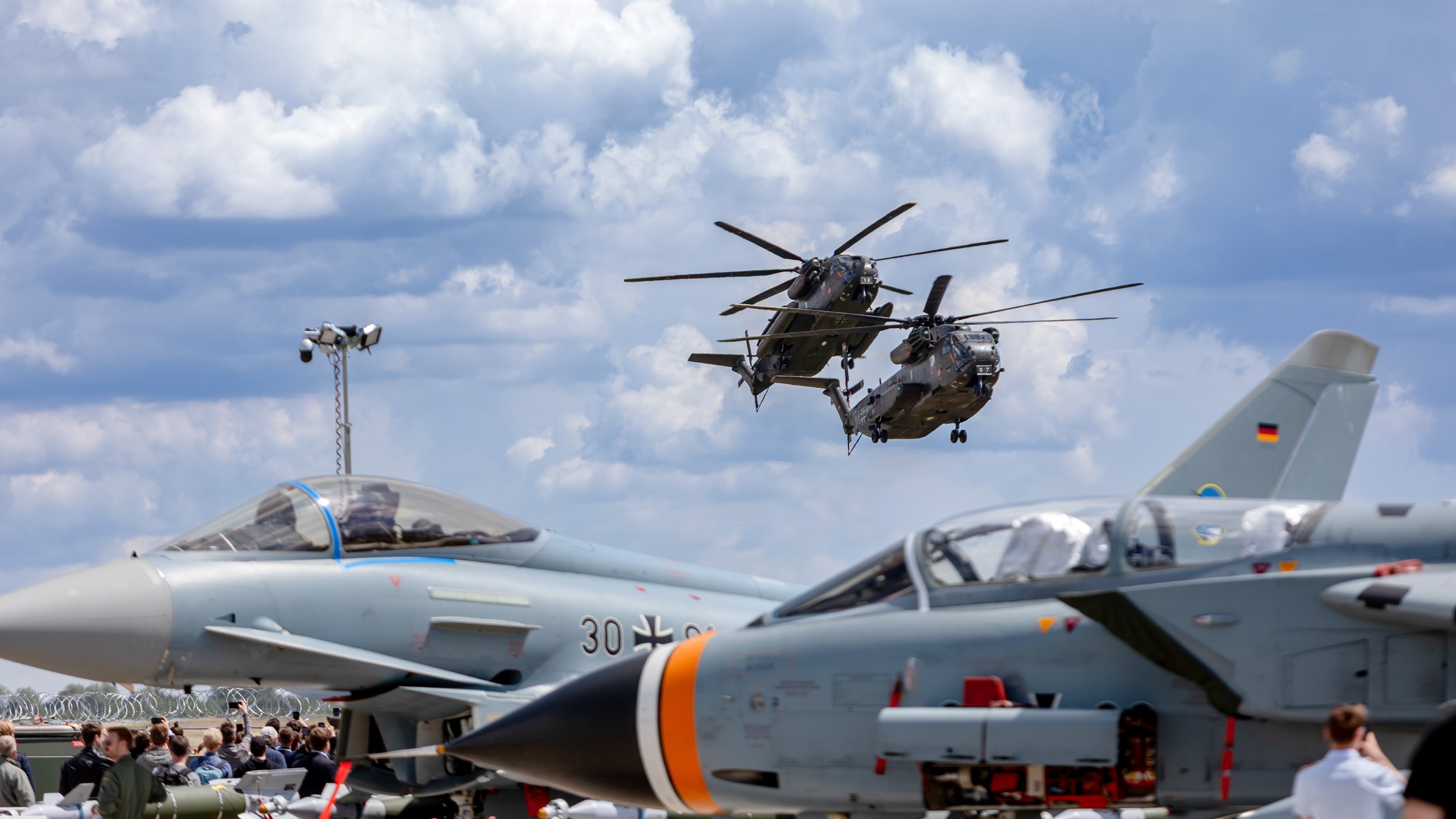 Two Bundeswehr Sikorsky CH-53 helicopters fly close together against a cloud-filled sky during the flying display at ILA
