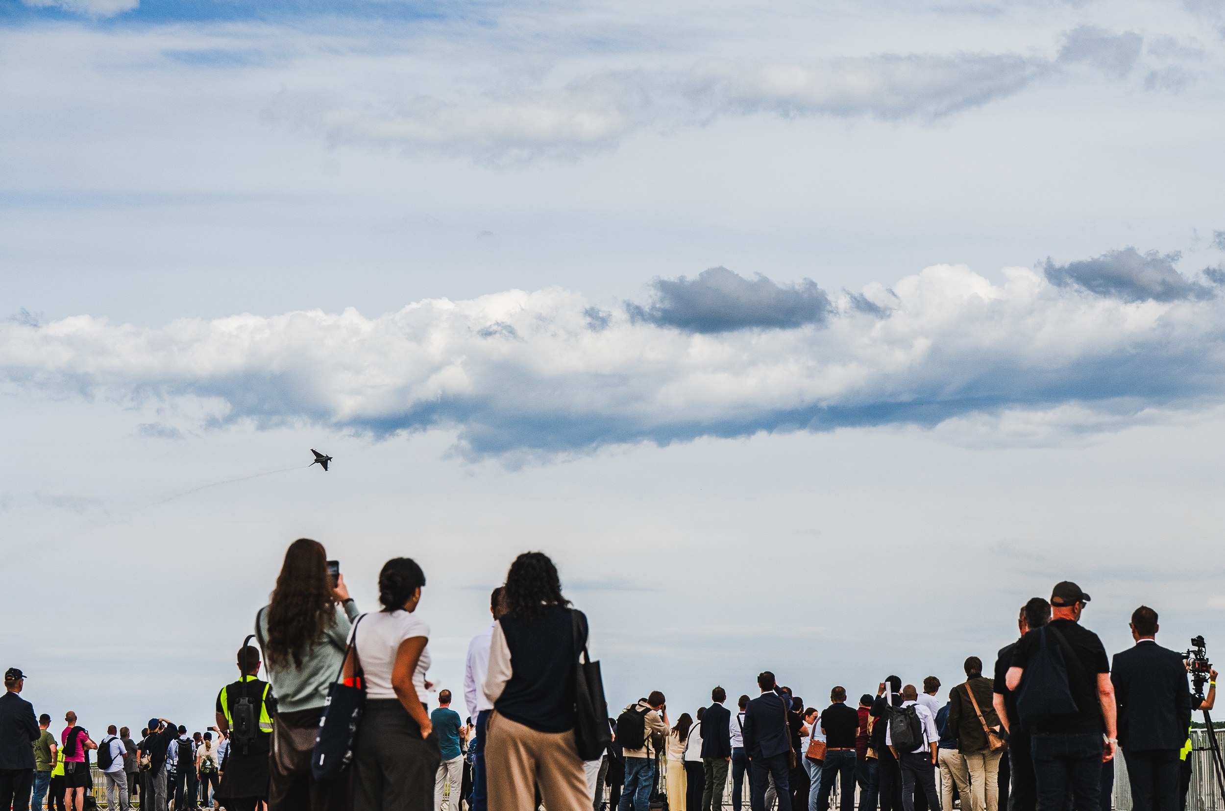 Eine große Besuchergruppe verfolgt das Flying Display der ILA Berlin 2026 vom Freigelände aus, viele halten Smartphones …