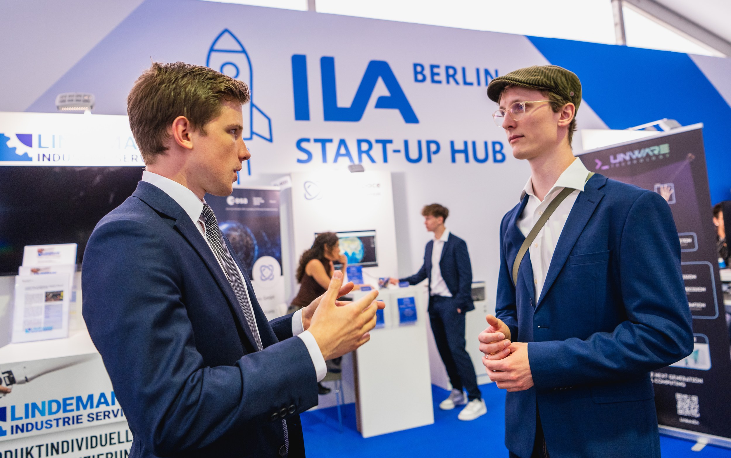 Zwei Männer stehen sich im Vordergrund des ILA Start-up Hub gegenüber und führen ein konzentriertes Gespräch.