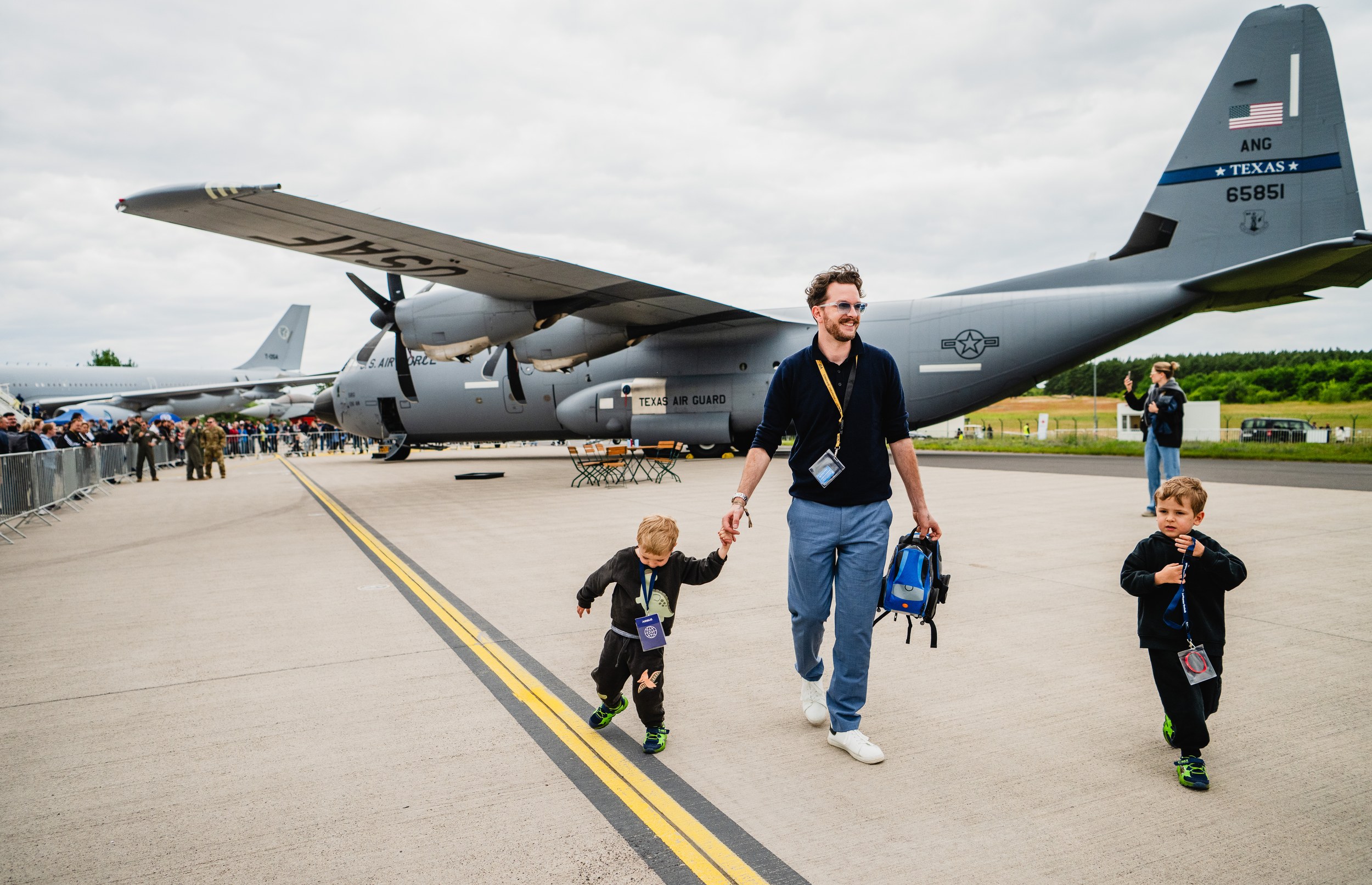 Ein Vater geht mit zwei kleinen Kindern über das Vorfeld vor einer grauen Lockheed Martin C-130 Hercules der Texas Air …